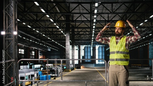 Male professional coordinating industrial operations with walkie-talkie, ensuring two-way radio communication between colleagues for efficient heavy industry manufacturing activity.