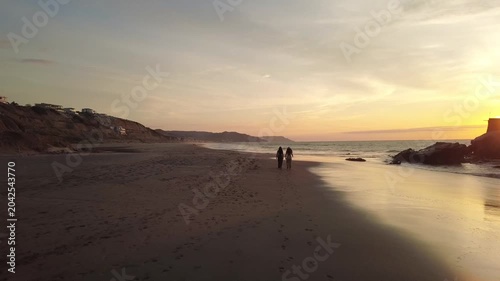 Tracking shot of two Ecuadorian girls walking along the coastal profile of Santa Marianita beach, Manta, right at golden hour, Ecuador, South America.