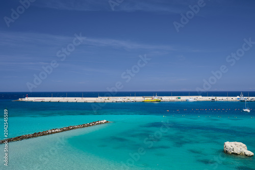 Harbour wall harbor wall in Puglia southern italy with single yacht turquoise sea and blue sky in summer