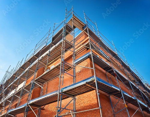 construction site facade with orange brick wall and metal scaffolding under clear blue sky showing building progress and structure