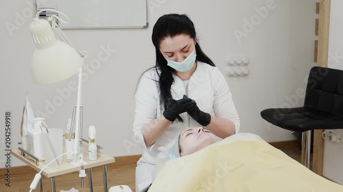 A female professional cosmetologist applies protective ointment to a client after a procedure