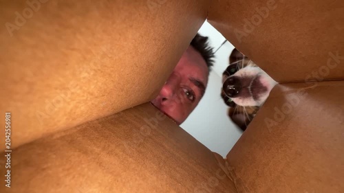 A man shows a dog a treat inside a box. View from inside.