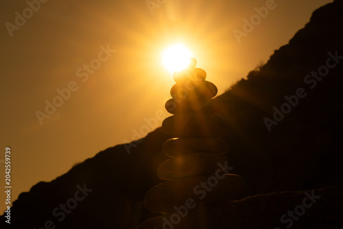 Canvas Print Cairn stones balance silhouette against dramatic golden sun flare during serene sunset over dark hillside