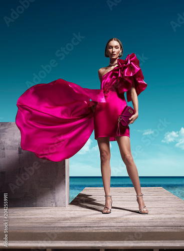 Fashion model in magenta satin dress with flowing train on wooden pier