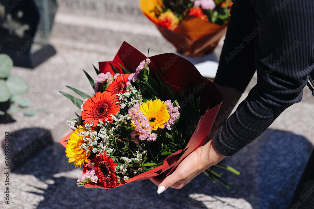 Obraz premium Woman placing flower bouquet on grave. Cemetery memorial visit. Remembrance and mourning tradition. Colorful flowers during commemoration ceremony closeup.