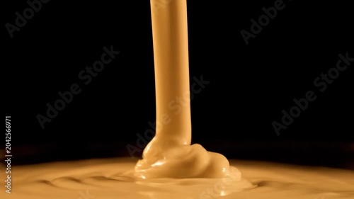 Smooth golden caramel sauce pouring and dripping onto a flat surface creating ripples and a rich glossy texture against a dark background
