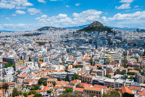 Elevated panoramic view of Athens from the Acropolis, with Lycabettus Hill rising in the distance under Mediterranean sky.