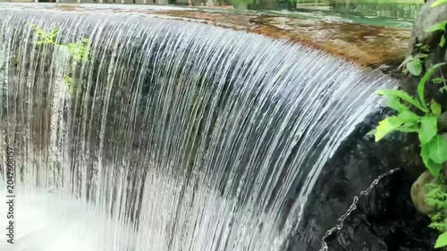 Flowing water over small dam or waterfall structure, natural freshwater movement creating relaxing and peaceful scenery.