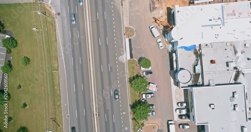 Cars drive along busy highway with commercial building on parking spaces are filled near building while present in surrounding area.
