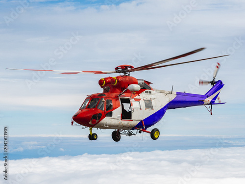 Red rescue helicopter flying above mountains and clouds.