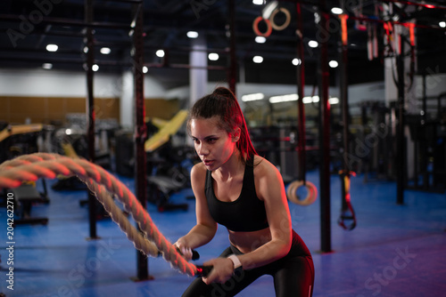 Determined female athlete exercising with battling ropes
