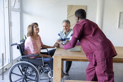 Cuadro en lienzo Diverse senior woman in wheelchair holding hand, aide in maroon scrubs placing p