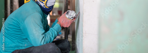 Photos Construction worker uses a handheld power sander to remove old paint dust from an aged wall
