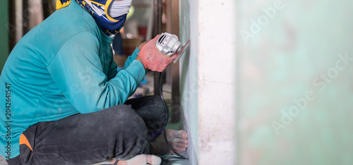 Quadro su tela Construction worker uses a handheld power sander to remove old paint dust from an aged wall