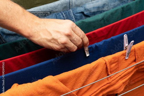 Hand clipping colorful clothes on drying rack