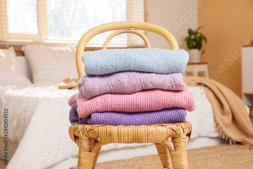 Stack of knitted sweaters on wicker chair in bedroom, closeup