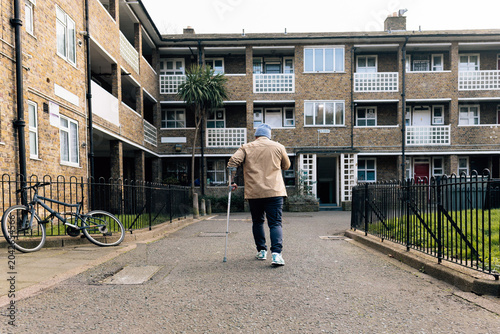 Individual with crutch walking towards social housing building