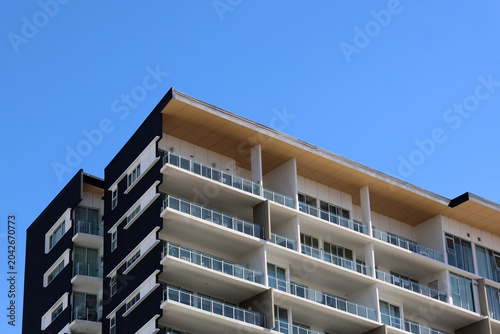 Modern multi-story apartment building facade featuring black and white balconies under a clear blue sky