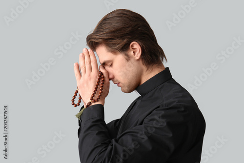 Foto Young priest praying with beads on dark background