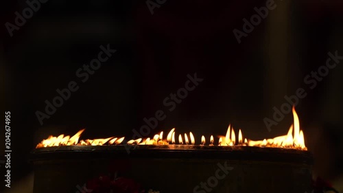 Rows of warm candle flames in a dark temple setting create a sacred visual composition with glowing light, soft smoke, and peaceful Buddhist worship atmosphere.