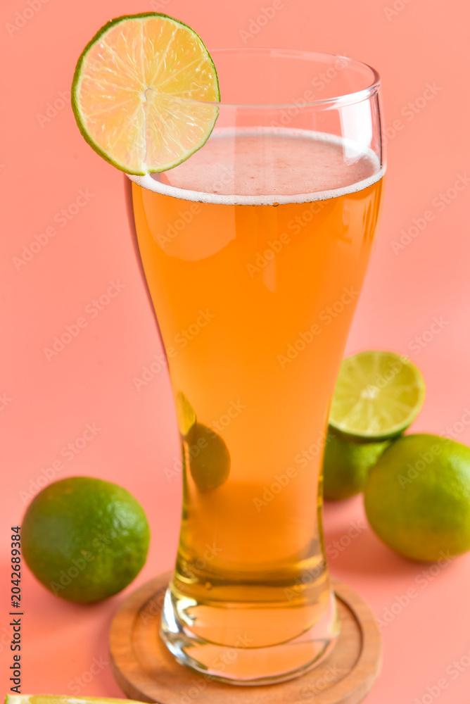 Fototapeta premium Glass of cold beer with lime on pink background