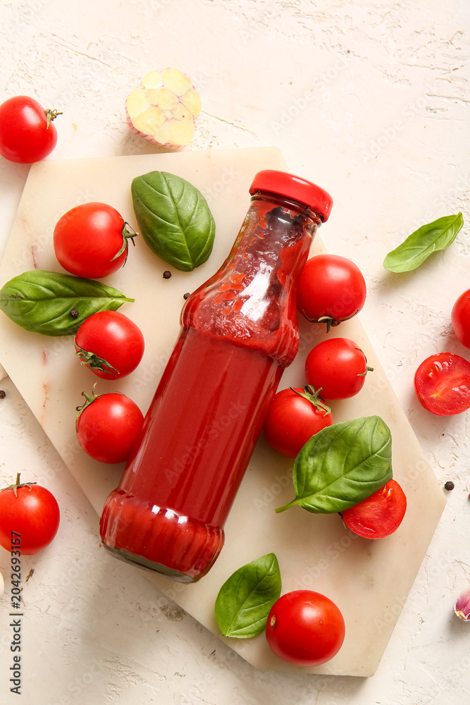Obraz premium Board with glass bottle of ketchup and tomatoes on white background