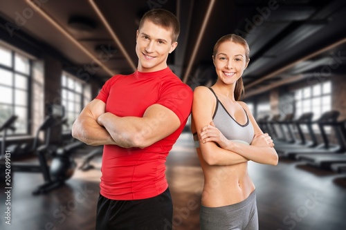 Fitness couple standing back to back with arms crossed in a modern gym interior