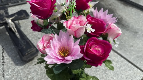 Artificial pink flowers on cemetery grave with cross