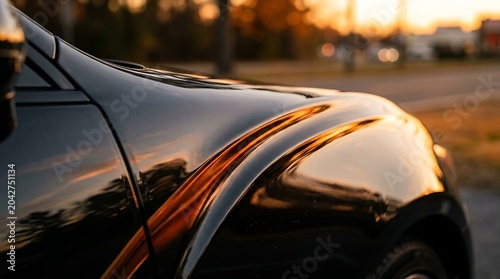 Close-up of a Sleek Black Car Fender Reflecting Golden Hour Sunset Light