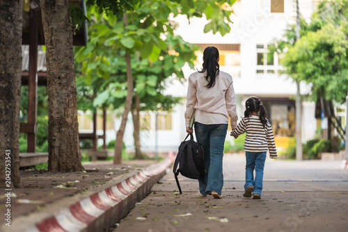 mother holding daughter's hand and walking together to school. First day of education.