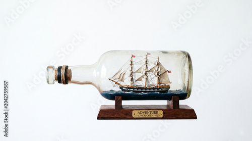 Miniature wooden sailing ship inside a glass bottle ornament, isolated on a white background. Traditional handicraft and souvenir concept
