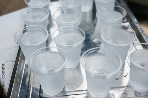 Fényképezés Clear plastic cup filled with cold water sits on shiny metal tray offering refreshing drink to quench thirst