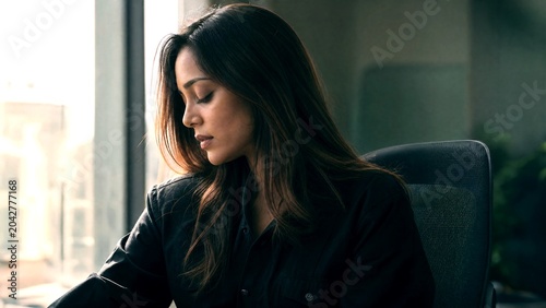 Professional business woman working in office, thoughtful female executive sitting at desk, corporate employee in modern workspace with window light