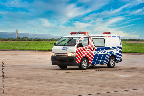 Medical rescue ambulance van driving on airport tarmac under blue sky