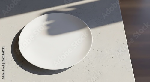 Empty white ceramic plate on a light gray speckled stone countertop with harsh diagonal shadows