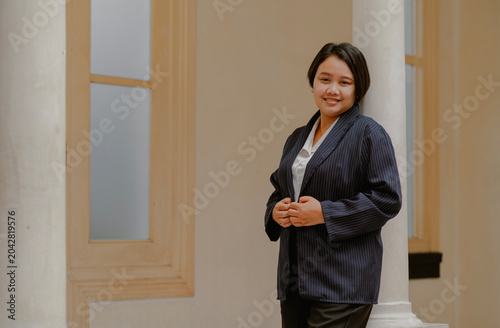 Smiling Asian Businesswoman with short hair adjusting a stripped black suit standing in a office building.