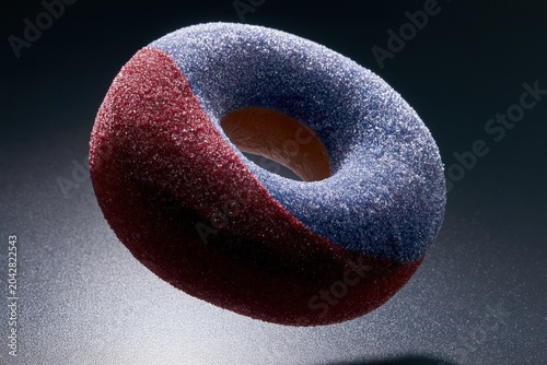 Sugared ring donut with blue and red coating floating against a dark background for bakery branding, confectionery editorial and food advertising with copy space