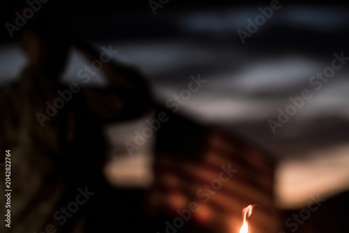 Silhouette of a person saluting against a flag and sunset sky for patriotic memorials, veterans day tributes and national holiday commemorative content with candlelight