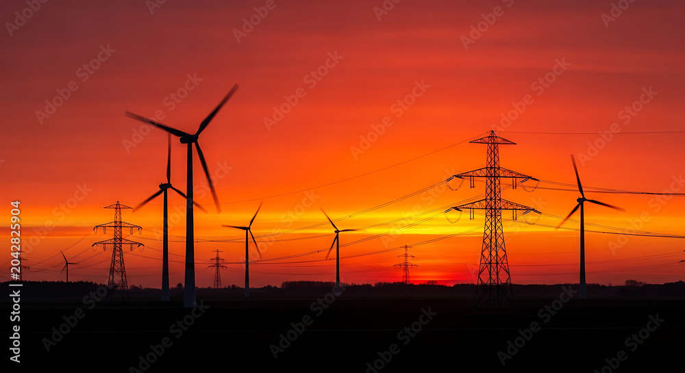 Obraz premium Wind turbines and electrical power lines at sunset with orange sky, turbines