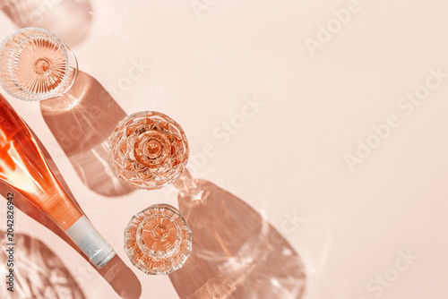 Wine Glasses and bottle of rose wine on pink background, sun glare and reflection from sun. Aesthetic composition from crystal glasses, sparkling alcohol drink, champagne, Summer romantic setting