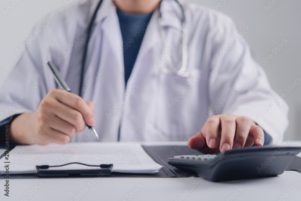 Fototapeta premium Professional physician in white coat calculating medical fee evaluating health insurance premium and writing clinical report on paperwork showing healthcare financial management concept