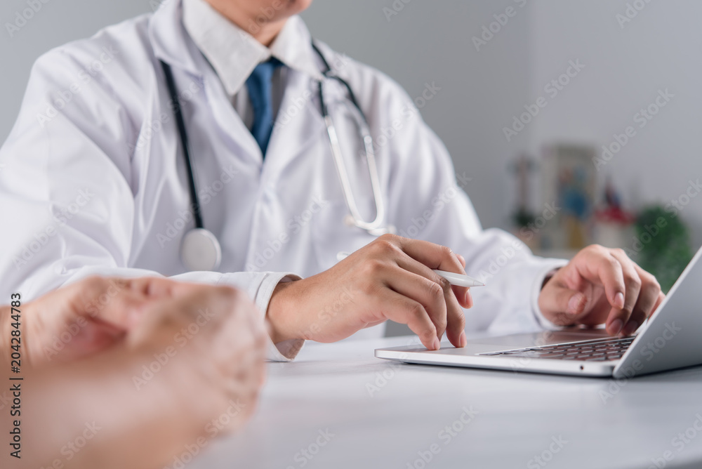 Obraz premium Modern medical healthcare concept showing professional physician using computer typing digital patient data while explaining treatment plan and health advice to elderly person at hospital desk