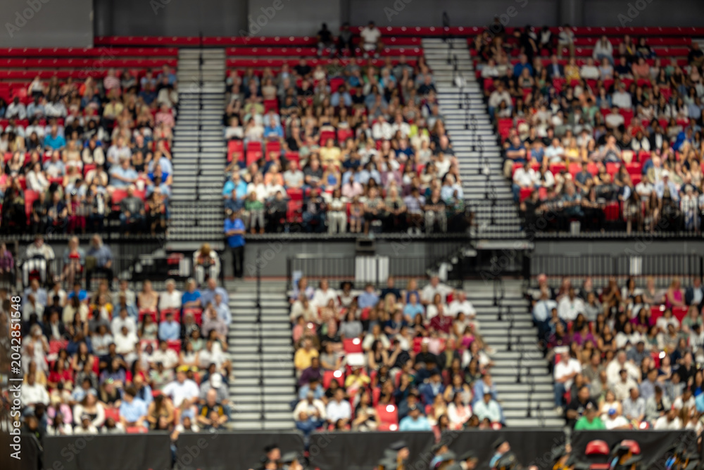 Obraz premium Blurred crowd of spectators sitting in stadium stands during large public event with shallow depth of field and abstract audience background