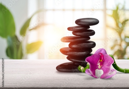 Canvas Print Black zen stones stacked with pink orchid and bamboo on a table in a bright spa