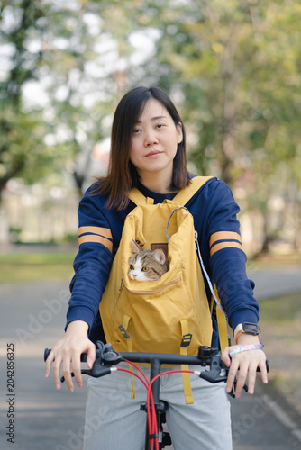 asian woman biking bicycle with her cat in backpack at park