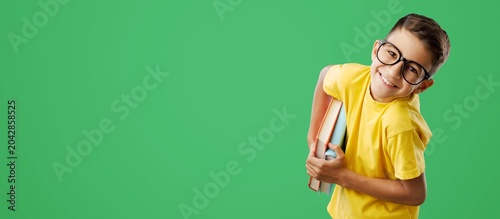 Tableau sur toile A happy schoolboy with glasses holding books against a green background with cop