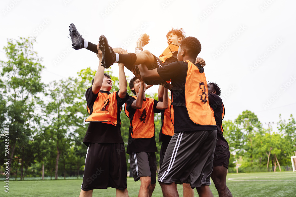 Fototapeta premium Diverse soccer players lifting their teammate up in celebration. Teamwork, victory and success concept during a football match.