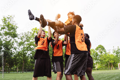 Tableau sur toile Diverse soccer players lifting their teammate up in celebration