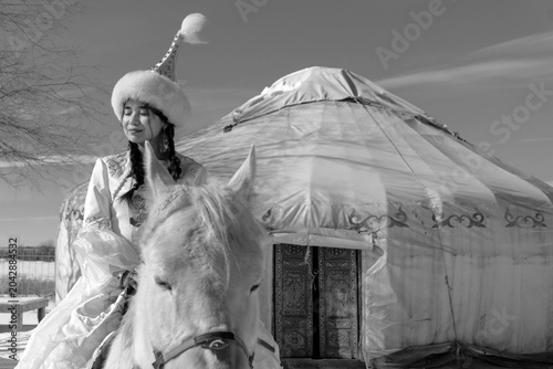 Obraz na płótnie Young Kazakh woman in traditional national clothing sitting on a horse, showcasing nomadic culture and heritage of Kazakhstan