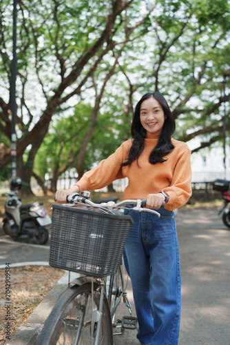 Young asian woman standing with bicycle in park smiling